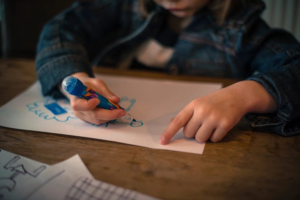 Mano de un niño pequeño dibujando con un marcador sobre papel